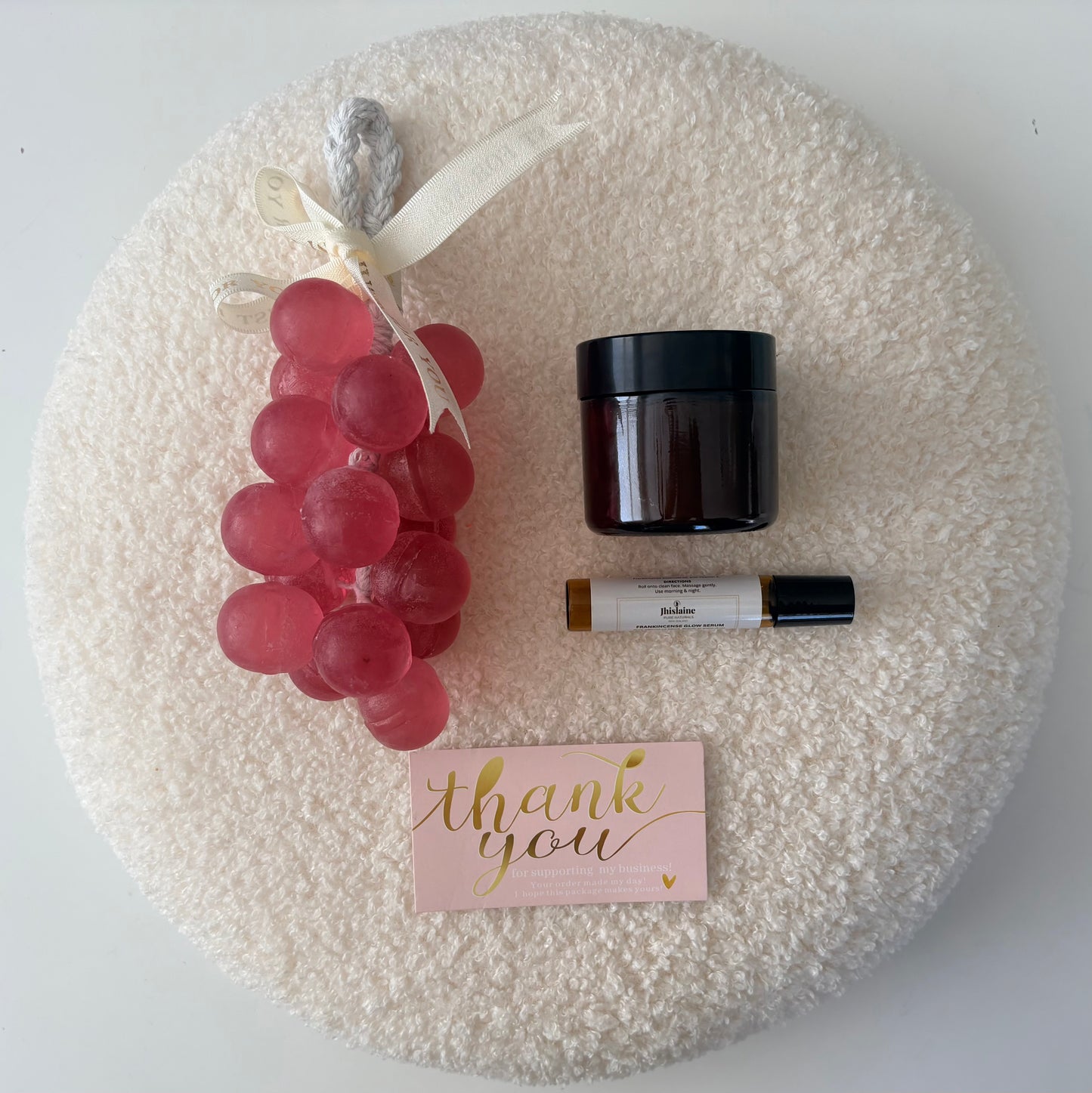 Decorative wreath with grapes, a jar, a bottle, and a 'thank you' card on a textured surface.