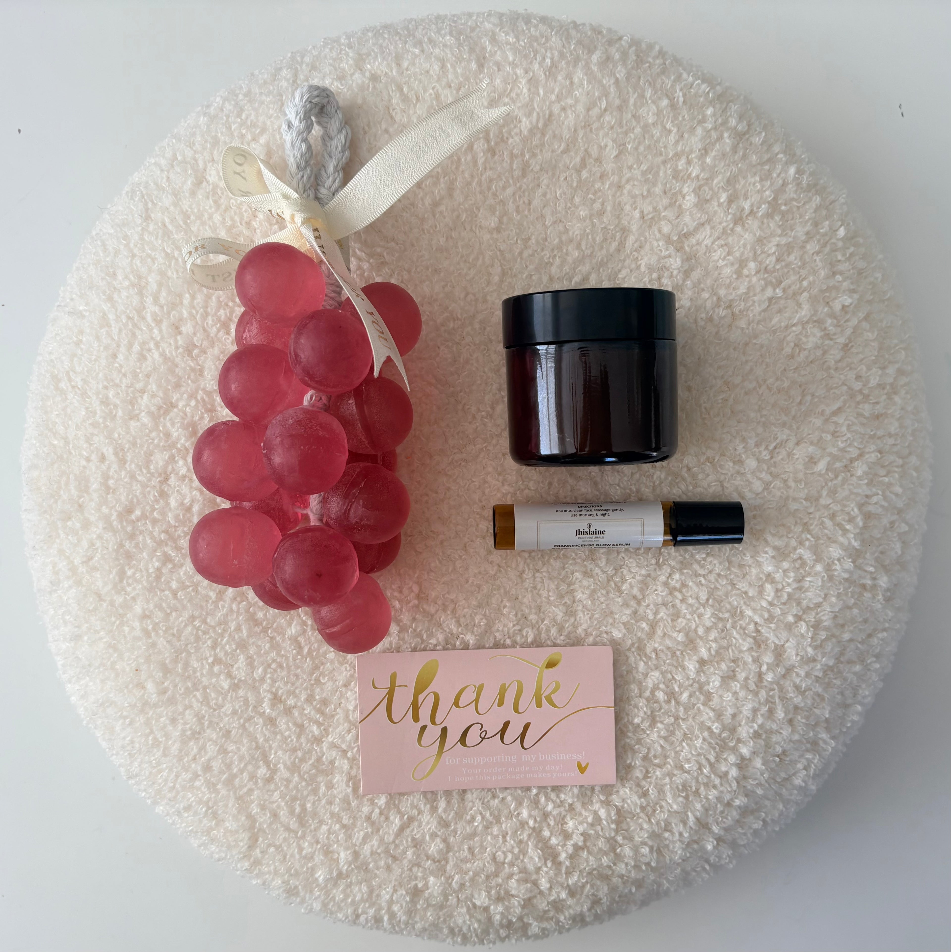 Decorative wreath with grapes, a jar, a bottle, and a 'thank you' card on a textured surface.